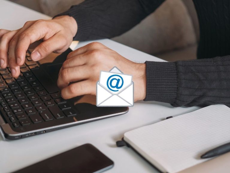 Close-up of hands typing on a laptop with a notepad and smartphone on a desk with an email notification.