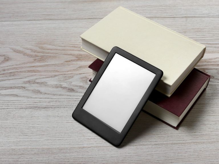 E-reader stacked on hardcover books on a wooden surface emphasizing how PLR Marketing Digital combines traditional and modern approaches to content.