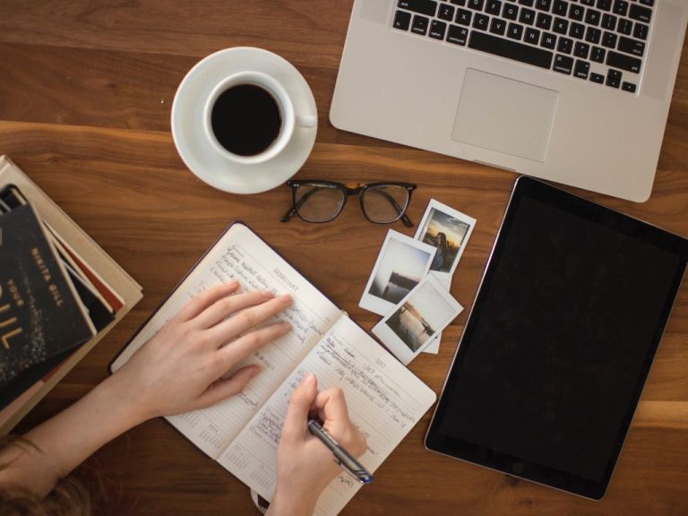 Workspace with a laptop, coffee, and an open notebook filled with handwritten notes or writing a letter.