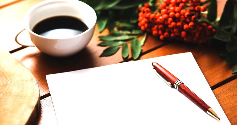 Get paid to write letters-Red ballpoint writing pen on blank paper with a coffee cup and decorative berries on a wooden table.