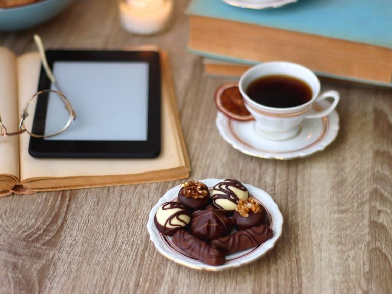 Person holding a Kindle with an e-book displayed, surrounded by books and coffee.