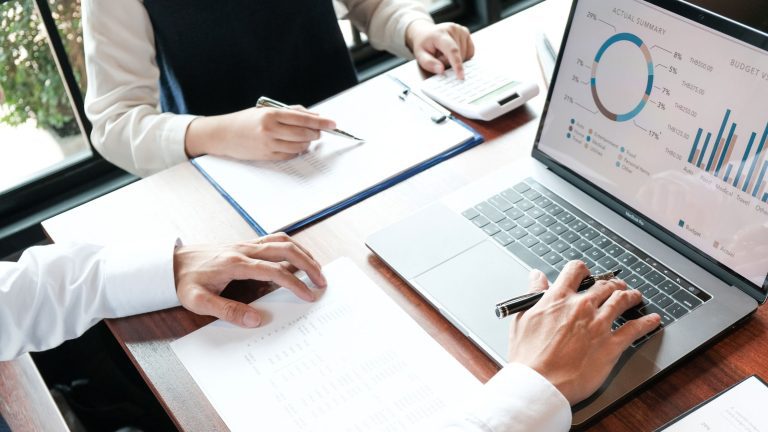 Two professionals analyzing charts and data on a laptop, with notes and calculators on the table, representing financial and affiliate marketing strategies.