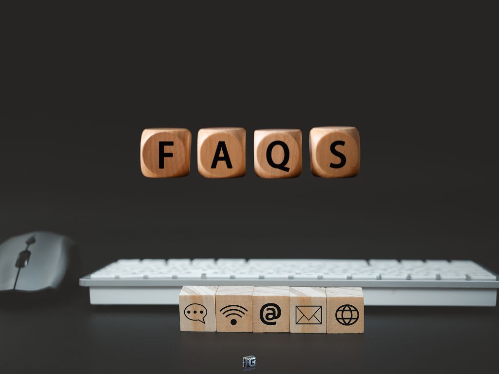 “Wooden blocks spelling ‘FAQs’ with communication icons and a keyboard and mouse in the background, symbolizing frequently asked questions about writing side hustles.”