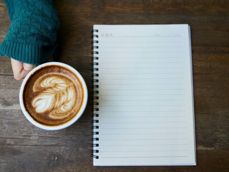 A blue vintage typewriter with a coffee cup, an open book, and a pen on a wooden desk.