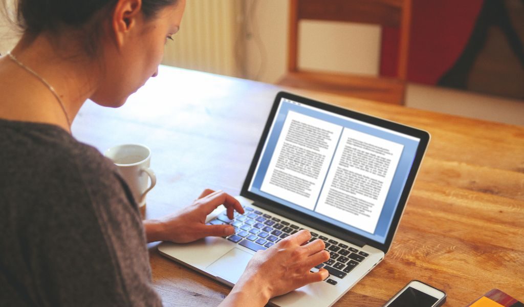 A woman typing on a laptop with an open document, representing freelance writing or remote work.
