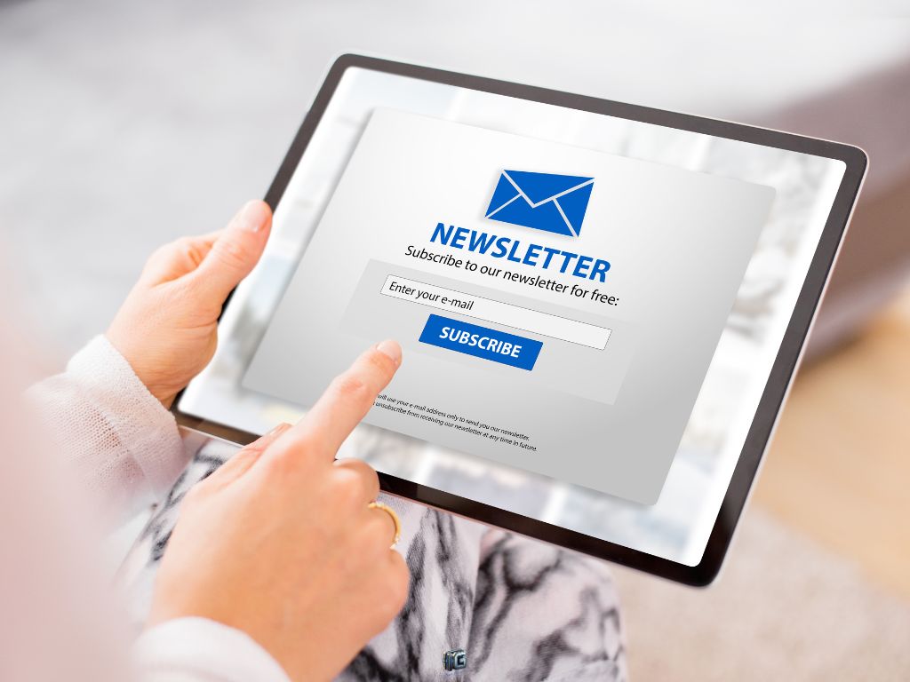Person using a tablet to subscribe to a newsletter with an email opt-in form on screen.