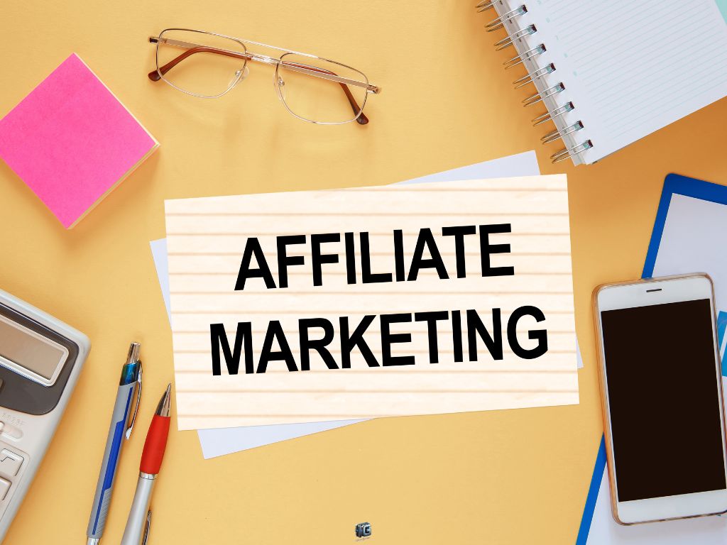 Top-down view of a workspace with “Affiliate Marketing” sign, notebook, smartphone, pens, and office supplies.